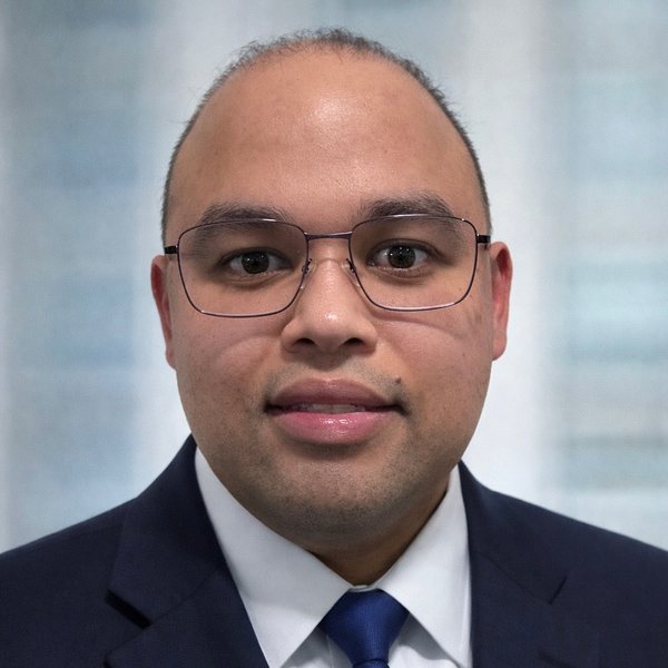 Headshot of Dr. Hasan Ahmad wearing glasses, a navy suit, white shirt, and blue tie