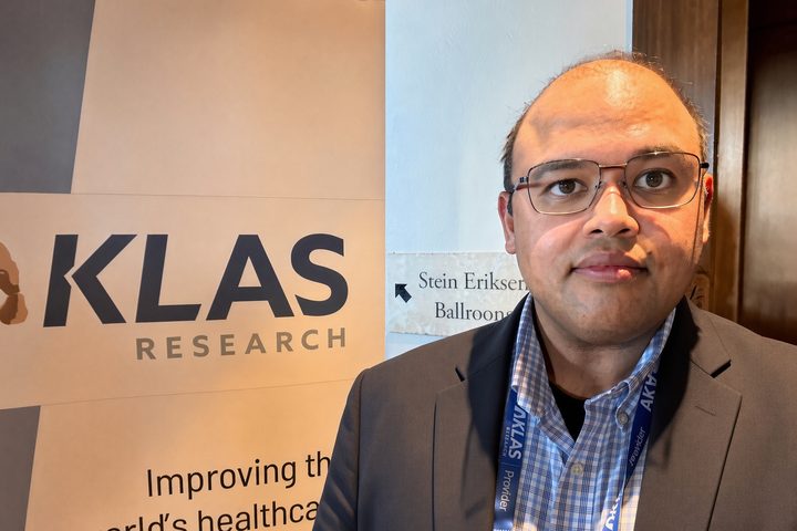 Hasan Ahmad wearing a KLAS Provider lanyard, standing beside a KLAS Research banner with a “Stein Eriksen Ballrooms” sign behind him.