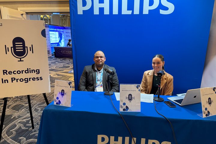 Hasan Ahmad and a host seated at a Philips-branded table with microphones and “Recording in Progress” podcast signs at a conference.